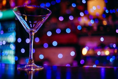 clean empty cocktail glass martini on a dark bar counter with a background of neon lights and bokeh