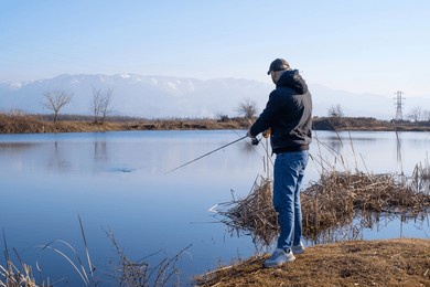 fishing with a spinning rod. a man fisherman catches fish with a spinning rod on a lake against the background of snow-capped mountains and a blue sky in autumn on a sunny day