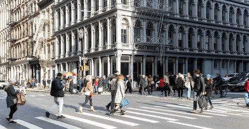 crowds of people at the busy intersection of broadway and broome street in the soho neighborhood of new york city with historic old buildings in the background cityscape