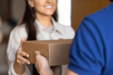 female customer taking parcel from delivery logistic service worker man, receiving ordered purchase, smiling, standing at home entrance. courier giving package to recipient cropped shot