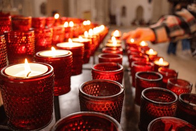 red candles burning in the church,  hand is visible lighting a candle, symbolizing prayer, hope and memory,  warm glow of the flame and the atmosphere of prayer