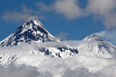 beautiful volcanic landscape: view on cone kamen volcano and erupting active klyuchevskoy volcano above the clouds. russia, far east, kamchatka, klyuchevskaya group of volcanoes.