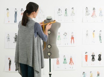 young caucasian female fashion designer taking measurements on mannequin in her studio