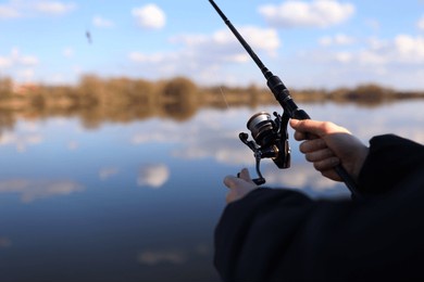 man catching fish, pulling rod while fishing from lake or pond. fisherman with rod, spinning reel on river bank. fishing for pike, perch, carp on beach lake or pond. wild nature, rural getaway