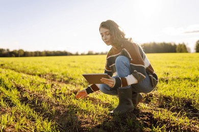 young woman farmer with modern tablet in green agricultural field. female agronomist working in field checking quality of green wheat. technology and farming concept.