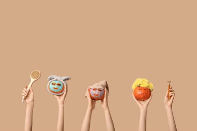 women holding funny pumpkins with cosmetic masks, massage tool and brush on color background