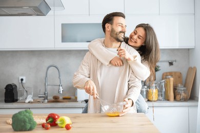 a couple embracing in the kitchen, embodying love and playfulness while preparing a delicious meal together with fresh ingredients.