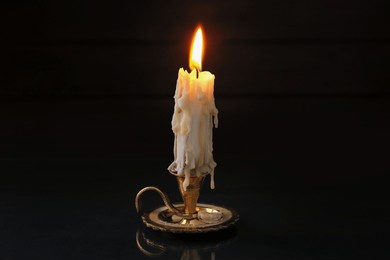 burning candle in candlestick on mirror surface in darkness
