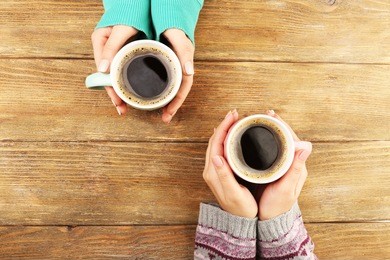 female hands holding cups of coffee on rustic wooden table background