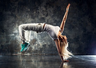 young woman modern dancer. on dark stone wall background.