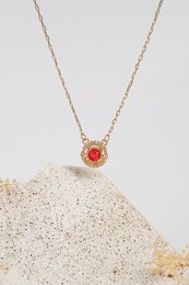 delicate gold necklace with red gemstone pendant displayed on textured stone and minimal white background