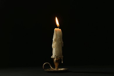 burning candle in candlestick on black background