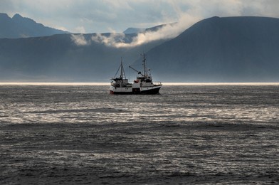 colorful fishing boats docked in a small norwegian village, framed by red wooden houses and dramatic mountain peaks in the background.