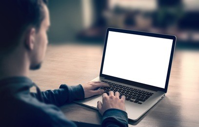 man using, working on laptop with blank screen in home living room.