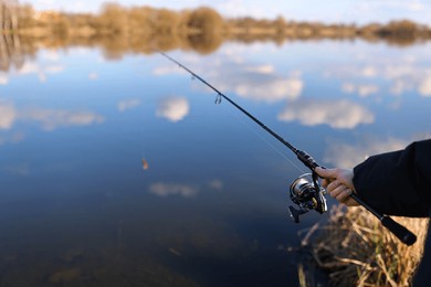 man catching fish, pulling rod while fishing from lake or pond. fisherman with rod, spinning reel on river bank. fishing for pike, perch, carp on beach lake or pond. wild nature, rural getaway