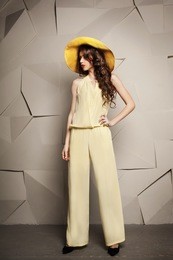 beautiful young woman with curly long brown hair standing in yellow hat and jumpsuit.  fashion model. stylish young people. young beautiful woman with long hair. beautiful hairstyle. yellow hat. 