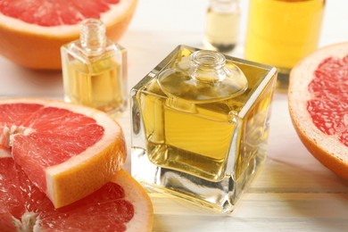 open perfume bottles with aromatic essential oils and slices of grapefruit on white wooden table, closeup