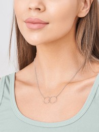 a model showcases a delicate layered necklace made of intertwined silver rings. she wears a casual mint green top, highlighting the simplicity of the jewelry in a bright setting.