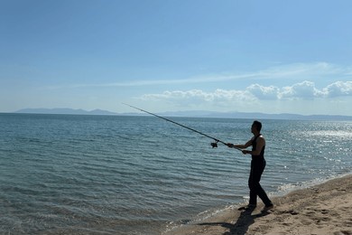 man fishing on beach at sunset, catching fish rod into calm sea or ocean, outdoor adventure, relaxing vacation, fisherman silhouette, fishing hobby concept. fisherman for pike, perch, carp.