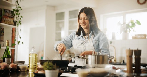 home, woman and chef in kitchen for cooking, culinary skills and ingredients on counter for dinner. house, happy person and cook with experience for food recipe, breakfast and meal prep on stove