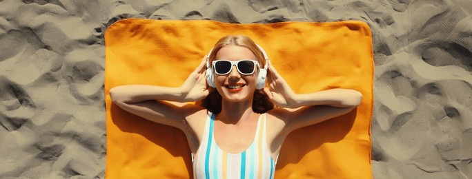 summer vacation, tourism, happy cheerful young woman listening to music lying on sand on the beach, relaxed tourist girl in headphones on towel in swimsuit, glasses, sunny day, top view