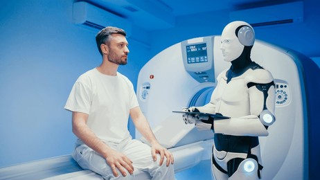 modern humanoid robot holding digital tablet and reviewing data while interacting with serious caucasian male patient. man sitting on scanner bed waiting for results as machine prepares procedure.