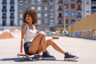 stylish young woman taking a break, sitting on her skateboard in a skate park, enjoying the urban environment