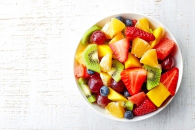 bowl of healthy fresh fruit salad on wooden background. top view.