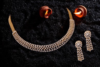 elegant diamond-studded gold necklace set with matching long earrings, displayed on black textured background with glowing diyas, perfect for festive or bridal wear.
