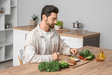 young man eating tasty fried egg with fresh avocado at wooden table in kitchen