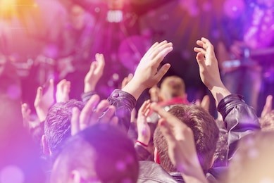 fans applauding to music band for live performing a concert on stage in open arena, selective focus toned image with sunflares.