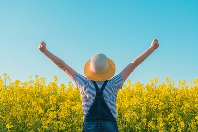 successful female farmer with hands raised in cultivated rapeseed field, selective focus