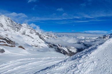snowy ski slopes and alpine peaks under a clear blue sky in saas-fee, switzerland, panoramic view of winter landscape with fresh snow, groomed pistes, and dramatic mountain scenery