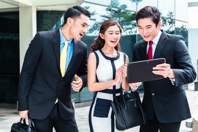 asian business woman and men working outside on tablet computer in front of tower building 