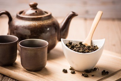 dry tea leaf in ceramic bowl wit pot on wood background