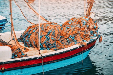 fishing nets with blue floats are lying on the bow of a small colorful fishing boat, gently floating on the calm water of a harbor