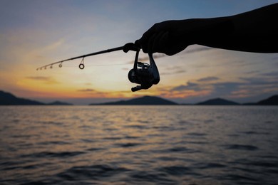 hand holding the fishing rod with sea background at sunset