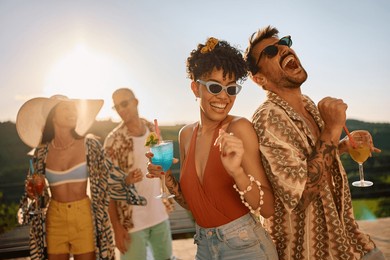 happy multiracial couple having fun in summer while drinking cocktails and dancing with friends on a patio.