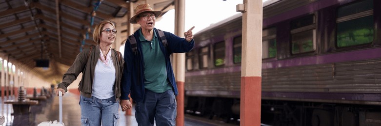 happy asian elderly couple enjoying travel adventure train station platform holding hands pulling luggage excited for journey.