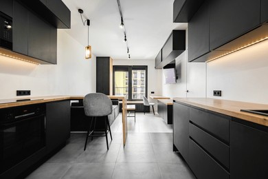 a contemporary kitchen showcases black cabinetry with wooden countertops, bright lighting, and an open layout in a stylish urban apartment, perfect for modern living.