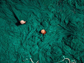 vietnamese workers preparing green fishing nets outdoors, hand traditional craft.