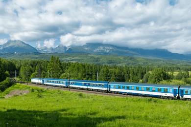 blue train passing through green fields with high tatras mountains in background, near strba, slovakia