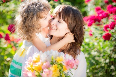happy woman and child with beautiful spring flowers against green background. family holiday concept. mothers day