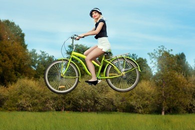 the girl on a bicycle in the park levitates over the meadow. she goes through the air without touching the ground.
