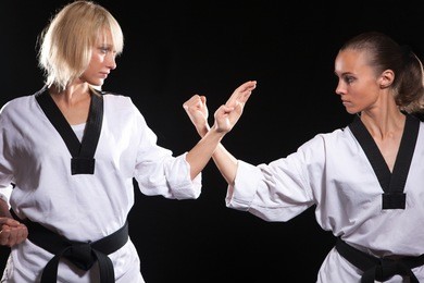 girls ready to fight,  because they taekwondo masters. two wemen stay in positions on black background