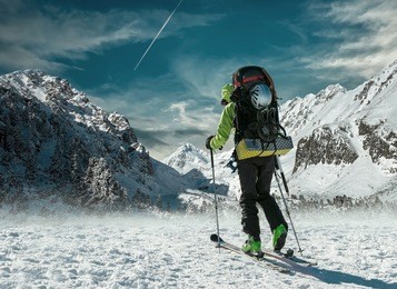 men with backpack at ski goes to the top of mountain in sun day