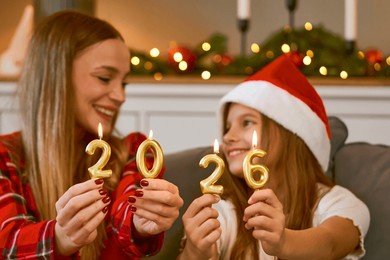 family share a festive moment at home, holding lit candle numbers 2026. warm lights, cozy decor, and holiday spirit highlight family, friendship, and celebration.