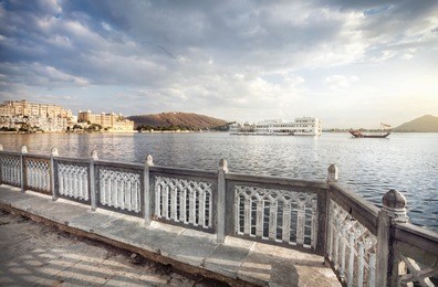 lake pichola with white palace in the center at cloudy sky in udaipur, rajasthan, india