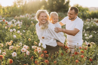 young family smiling, mother carrying toddler son on piggyback, father walking alongside in vibrant flower garden