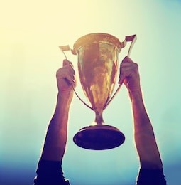 a man holding up a gold trophy cup as a winner in a competition toned with a retro vintage instagram filter effect app or action (backlit with the sun)